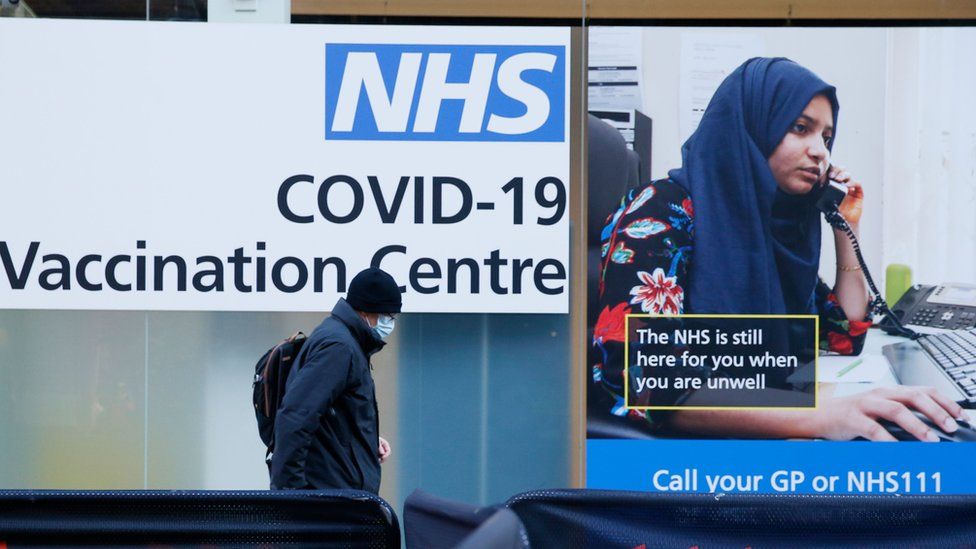 Man walks past NHS Covid-19 Vaccination centre poster