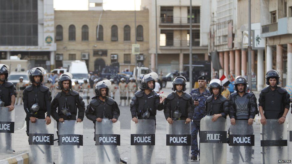 Riot police stand in front of protesters during a demonstration in central Baghdad on 9 August, 2015