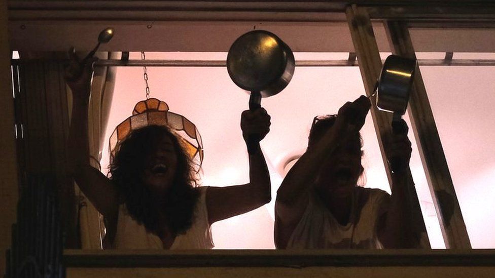 Women bang pots at the window of their apartment in Rio de Janeiro as they protest against Brazilian President Jair Bolsonaro over his handling of the coronavirus pandemic, 19 March 2020