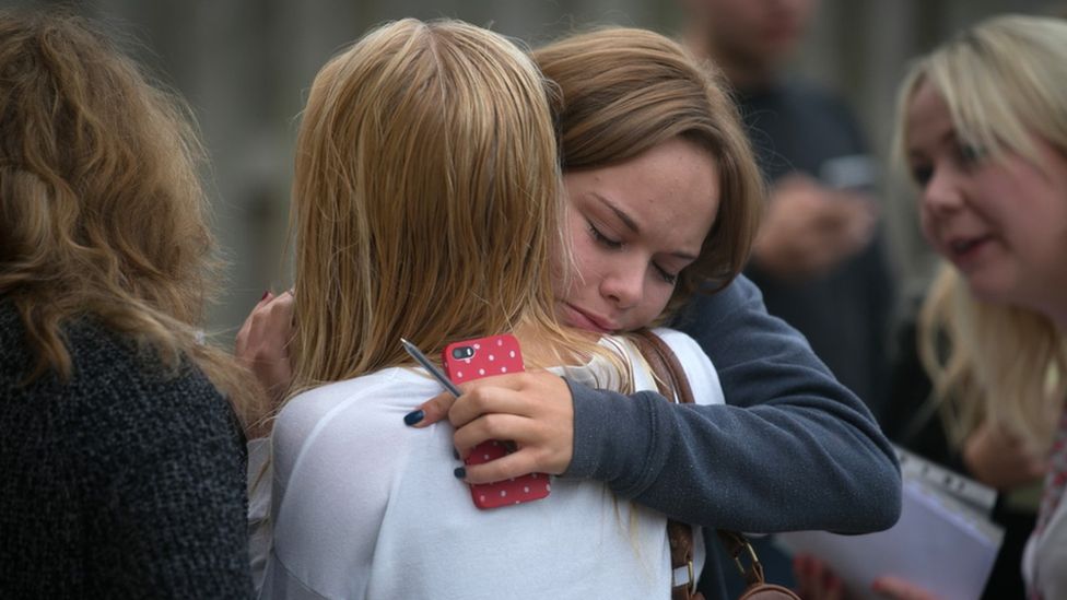 A young girl hugs her friend tightly after they receive their a-level results