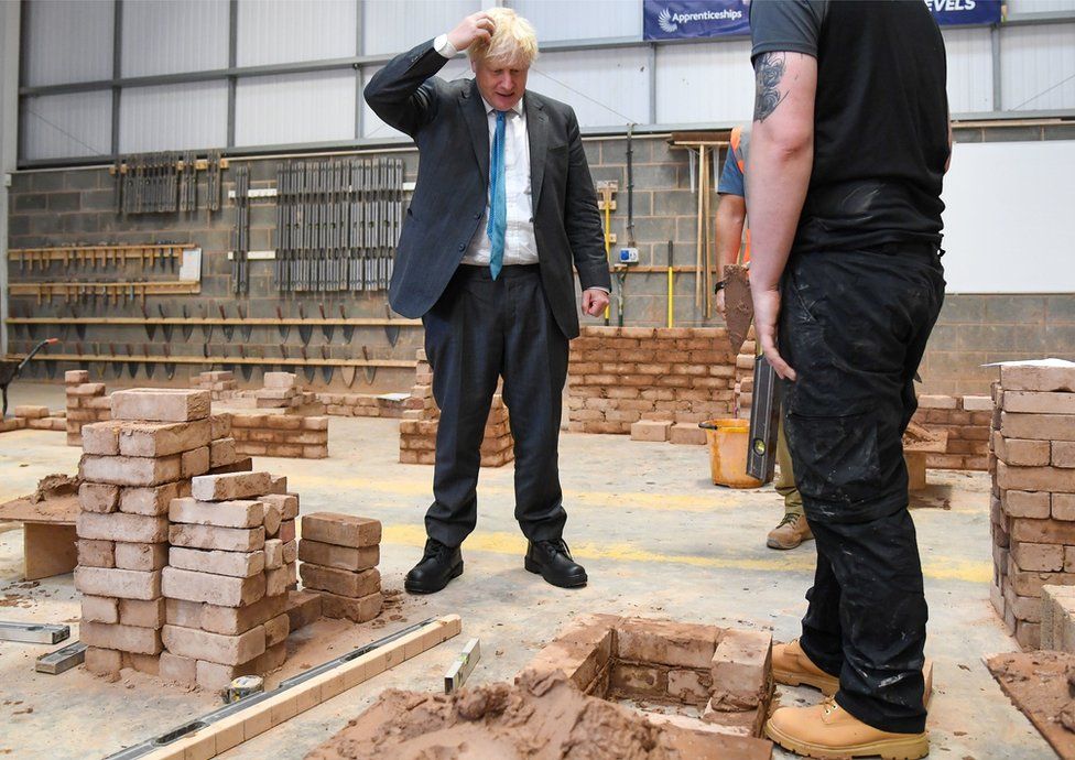 Prime Minister Boris Johnson is shown how to build a brick wall