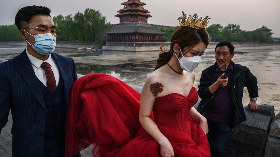 A Chinese man carries his future bride's dress while taking pictures in advance of their wedding in Beijing.