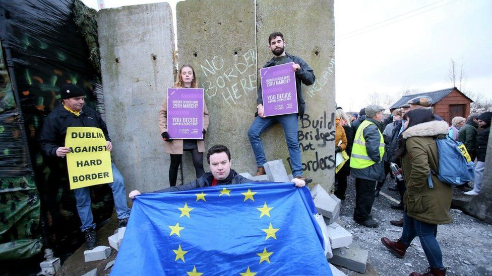 An EU activist holds an EU flag at a mock wall erected during a protest by an anti-Brexit campaign group on a road crossing between Northern Ireland and Ireland in Newry, Northern Ireland, on January 26, 2019
