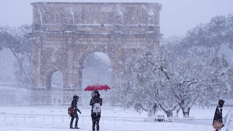 Tourists visit the Arch of Constantine during a snowfall in Rome