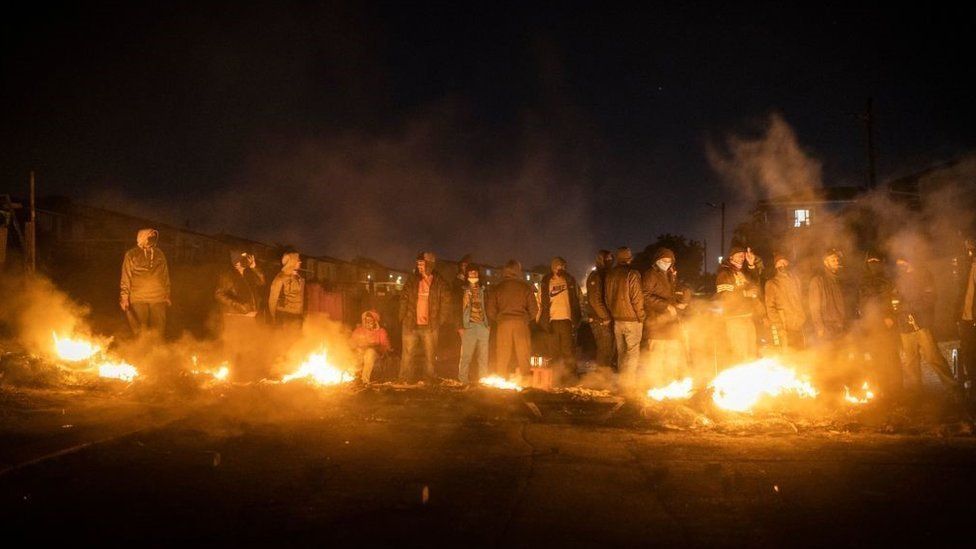 Armed community members gather around a fire to keep warm at a road block set up in Phoenix Township, North Durban, on July 15, 2021 to prevent looters from reaching the community.