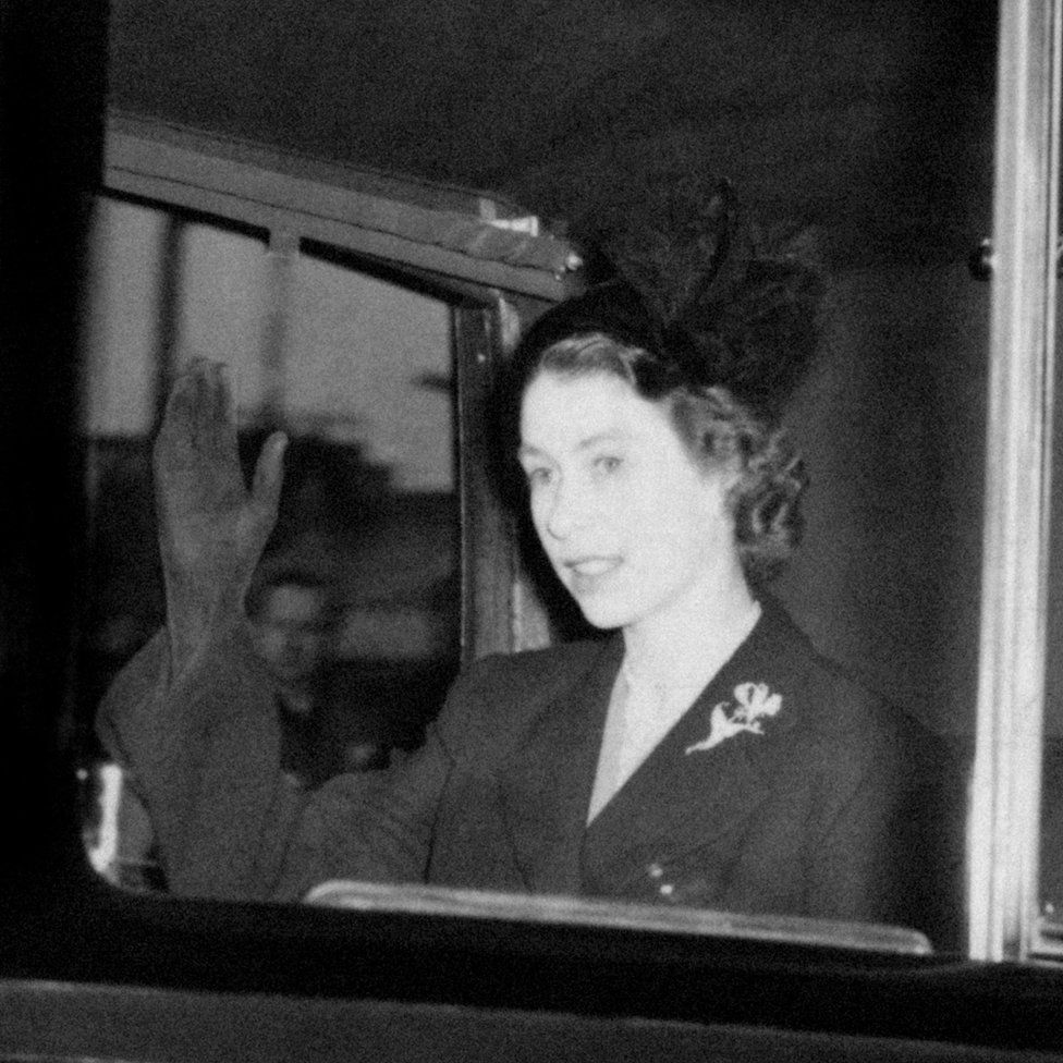 Queen Elizabeth II, in a black mourning outfit, waving as she returns to Clarence House in London the day after she became Queen. Princess Elizabeth, then just 25, was thousands of miles away in Kenya when her father King George VI died.