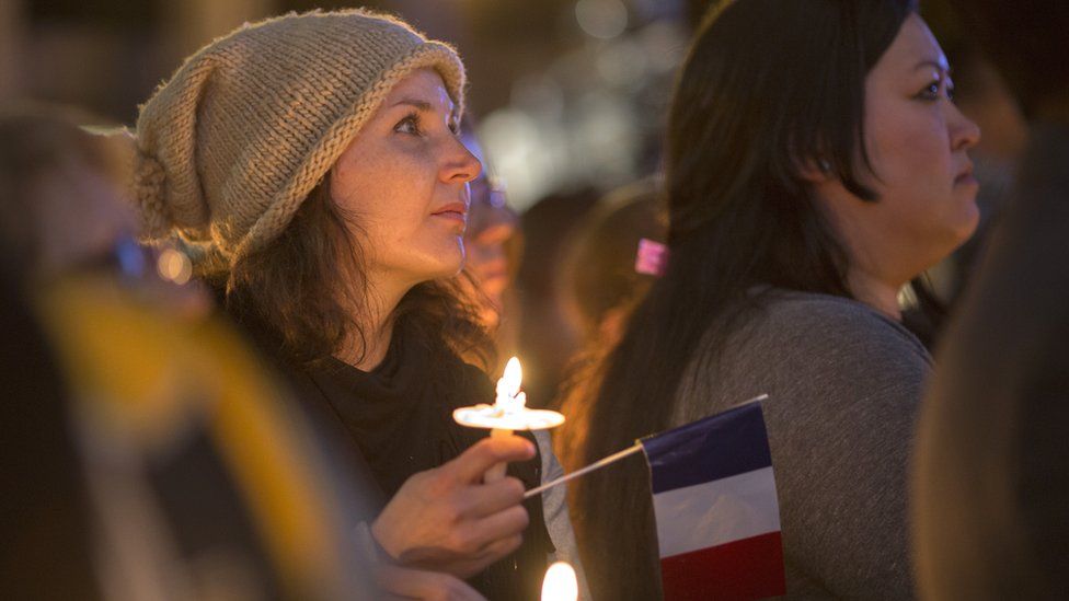 A woman holds a French flag at a memorial and vigil for the victims of the Paris attacks in 2015