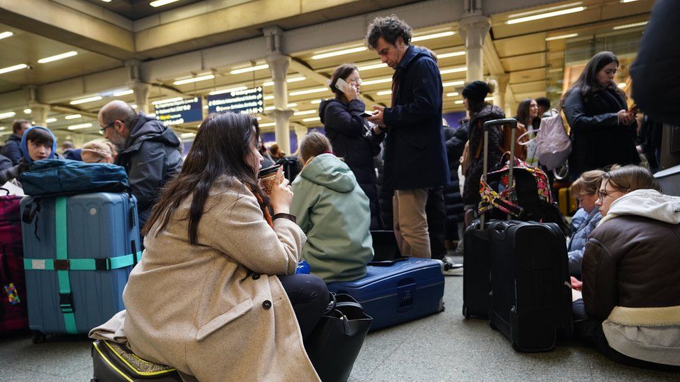 Passengers sit on the floor of the concourse at the entrance to Eurostar in St Pancras International station, central London, after high-speed services between London and Ebbsfleet were cancelled because of flooding in a tunnel under the Thames.