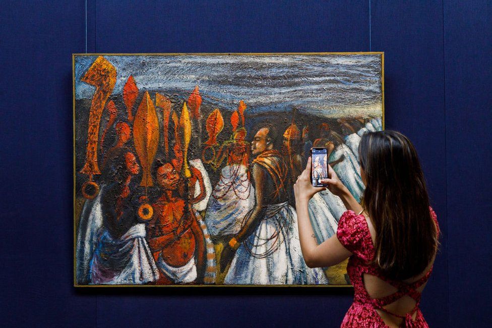 A woman takes a photo of Ben Enwonwu's The Court of the Oba of Benin.