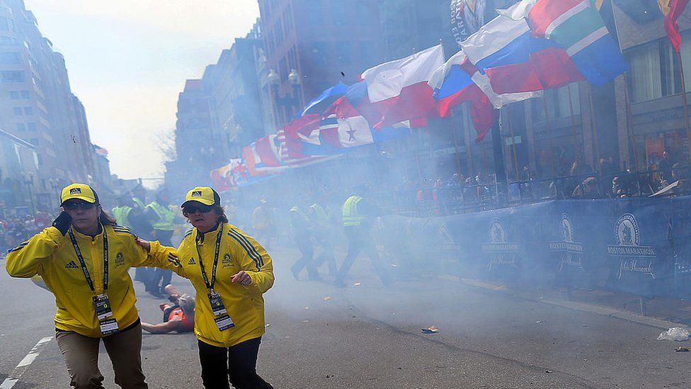 Официальный представитель гонки бежит из-под обломков, вызванных взрывом на Бостонском марафоне