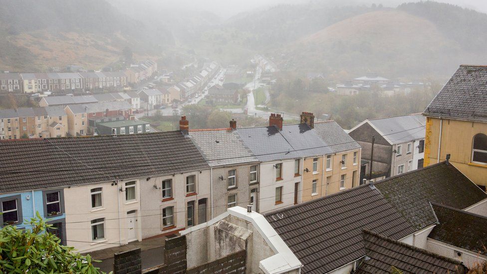 A townscape view of a welsh valley in the rain with the mountains and hills emerging out the rainy mirk. Rows of terrace houses and the edge of a chapel. A generic shot of the welsh valleys.