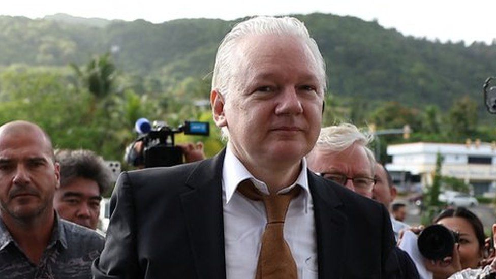 Julian Assange arrives at court in the Northern Mariana Islands surrounded by people