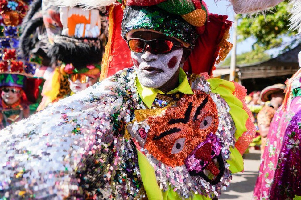 A man dressed in bright sequins, face paint and a large headdress.