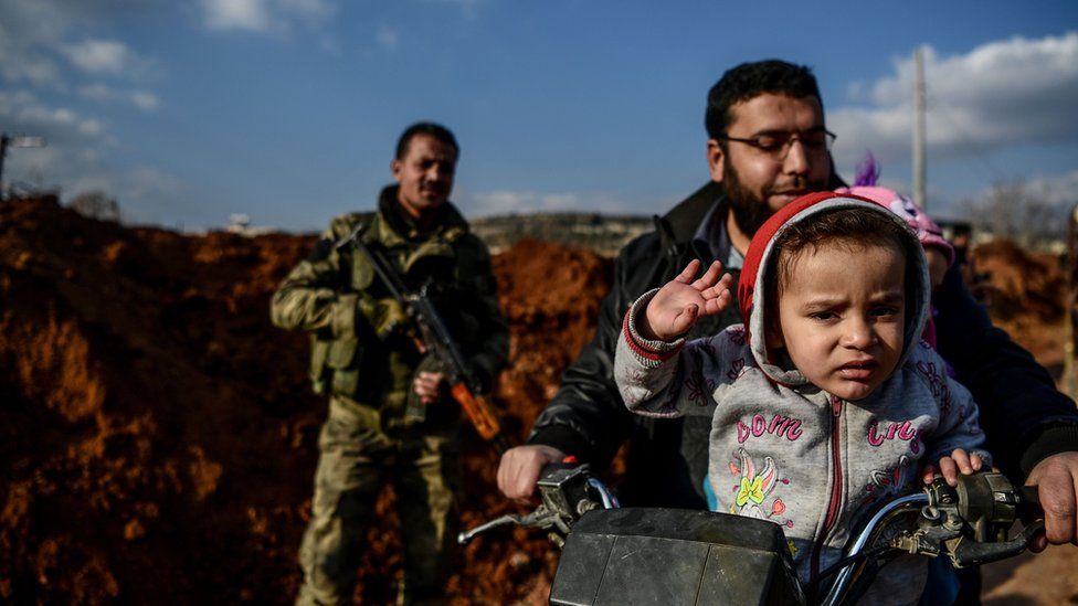 A Turkish-backed Syrian rebel fighter stands guard at a checkpoint as a family passes on motorbike in the Syrian town of Azaz on a road leading to Afrin, 1 February 2018