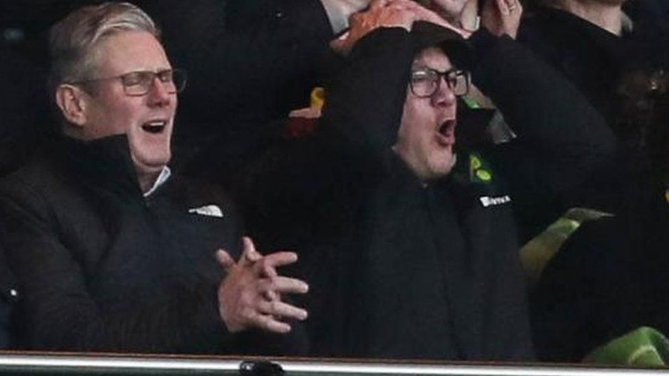 Sir Keir Starmer sitting alongside Ed Balls at a Norwich City match against Sunderland