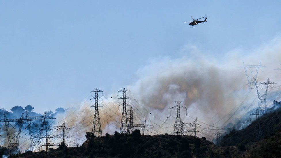 Helicopters fly over power lines engulfed in smoke