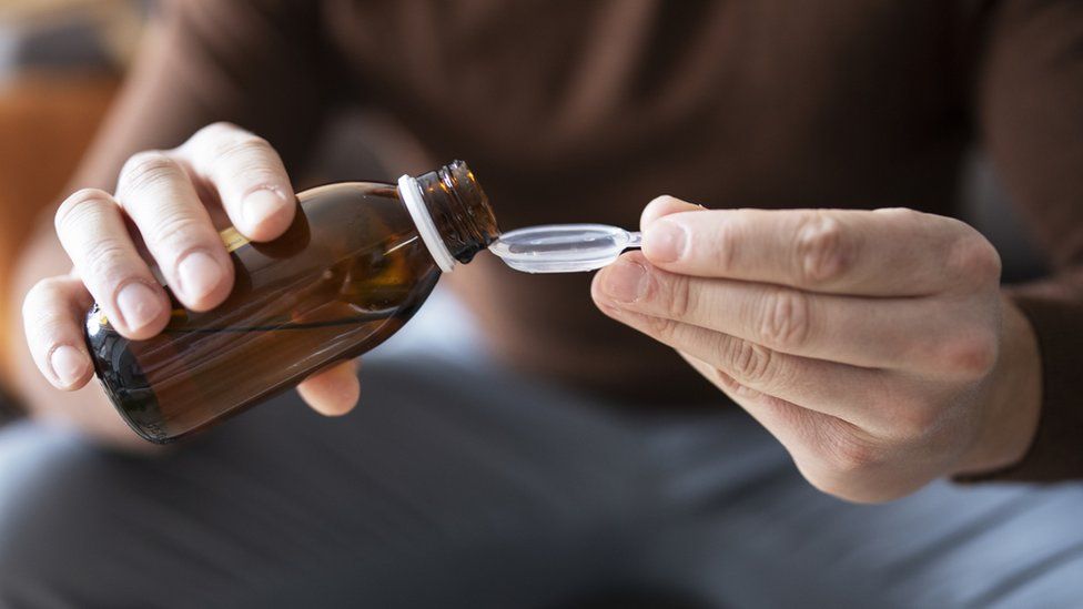 A man pouring cough syrup into a spoon