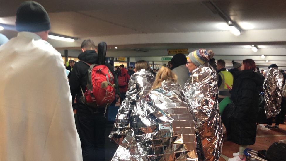 Passengers stood in the airport car park wrapped in emergency blankets