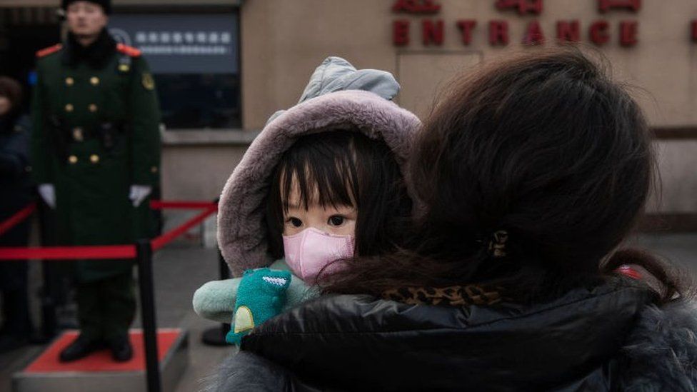 A Chinese girl wears a protective mask as she is held by a relative as they wait to board a train at Beijing Railway