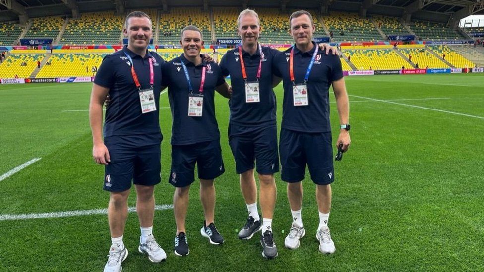 Tom Foley standing with three other match officials - all men are in the same navy kit