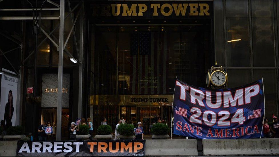 Banners reading 'Arrest Trump' and 'Trump 2024' outside of the Trump Tower building in New York City