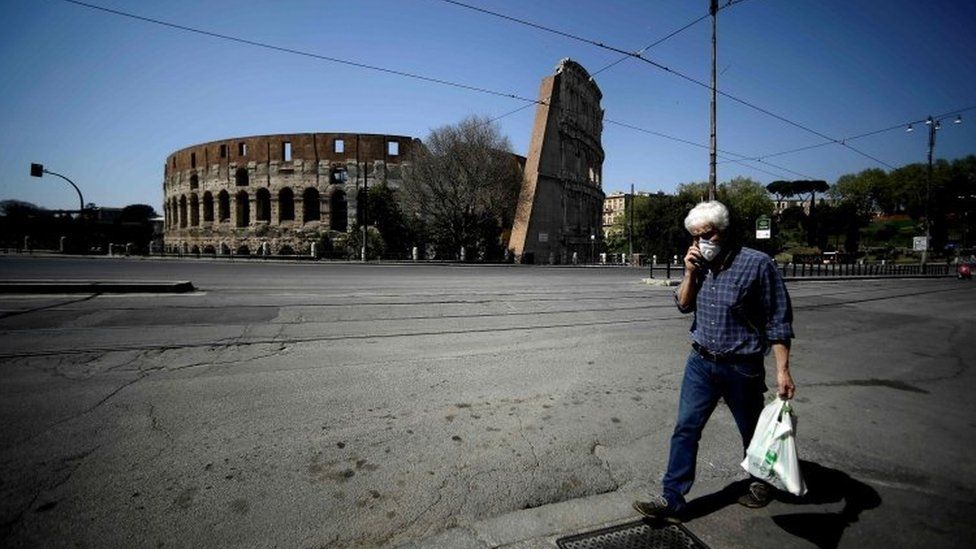 A man walks past the Colosseum in Rome wearing a face mask