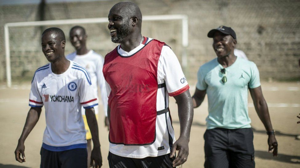 International Liberian football star, George Weah smiles with members of the opposite team after scoring a penalty during a match played on a dusty pitch at the Alpha Old Timers Sports Association in Paynesville in Monrovia on April 30, 2016
