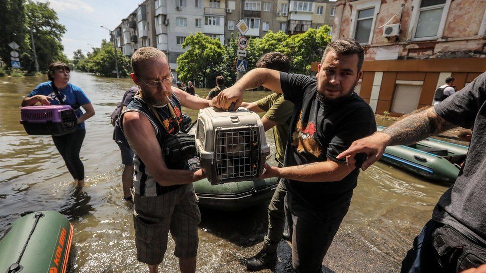 A man carries a dog in a cage in flooded Kherson