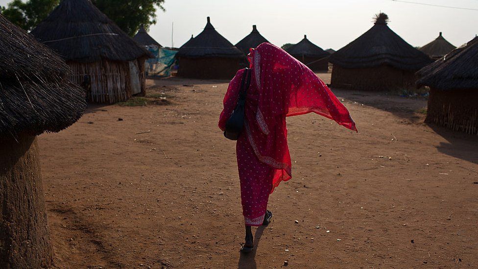 A Sudanese woman wearing pink walks through a village