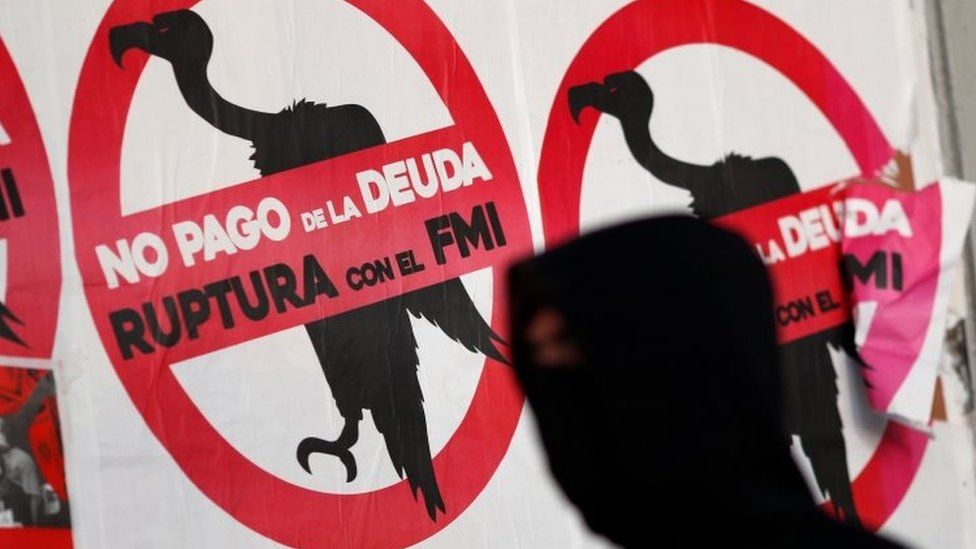 A pedestrian wearing a face mask, as a preventive measure against the coronavirus disease (COVID-19), walks past posters on the street that read "No to the payment of the debt. Break with the IMF"