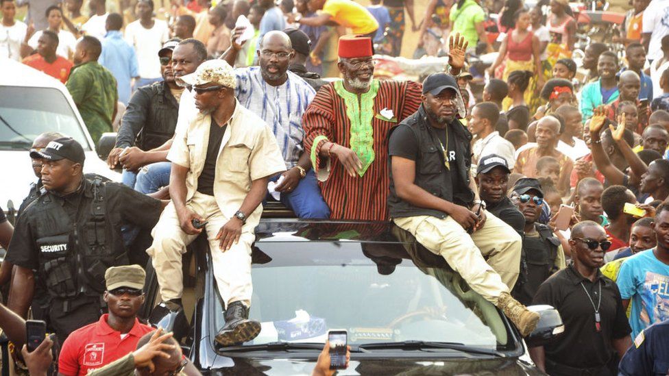 A picture taken on October 27, 2017 shows a leader of the MDR (Movement for Democracy and Reconciliation), ex-warlord Prince Johnson (R) waving to supporters on the top of a car with Liberian presidential candidate George Weah, whom he had endorsed, in Monrovia