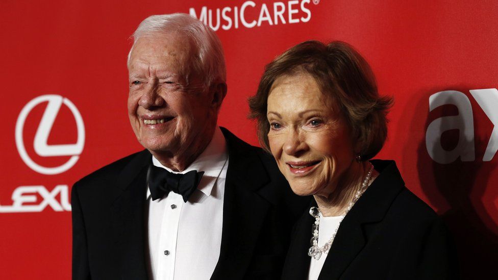 Jimmy Carter and his wife Rosalynn Carter posing in front of a red backdrop