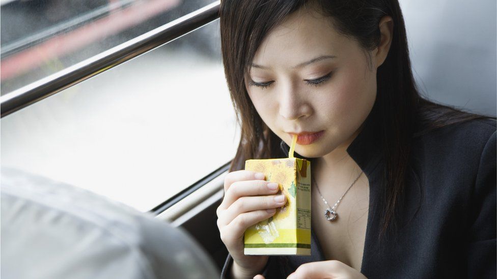 A woman sips from a drink carton with a plastic straw