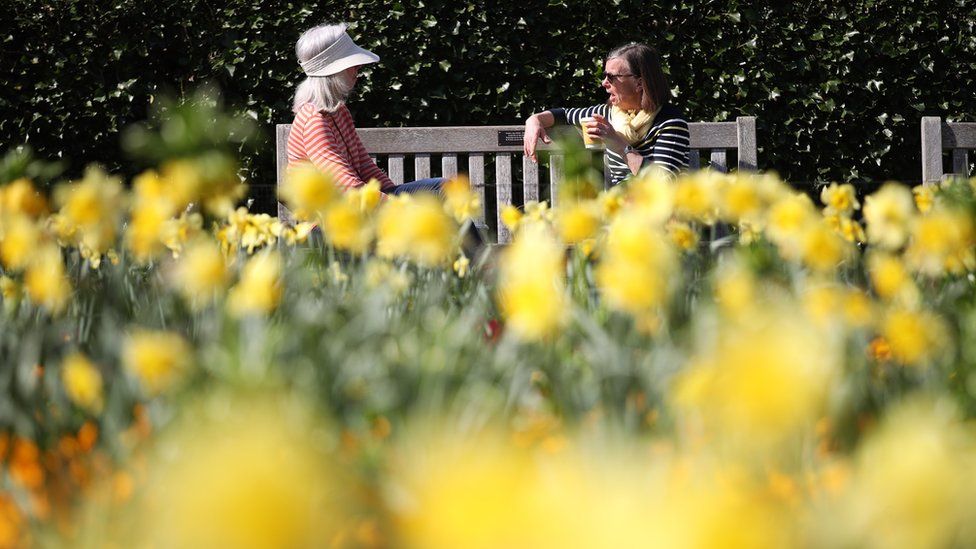 Two women visitors enjoying the sun at the Royal Botanic Gardens, Kew, in south-west London
