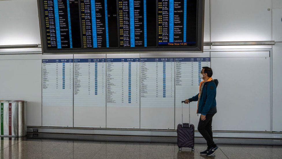 Мужчина с чемоданом проходит мимо табло с информацией о рейсах в международном аэропорту Гонконга в декабре 2022 года