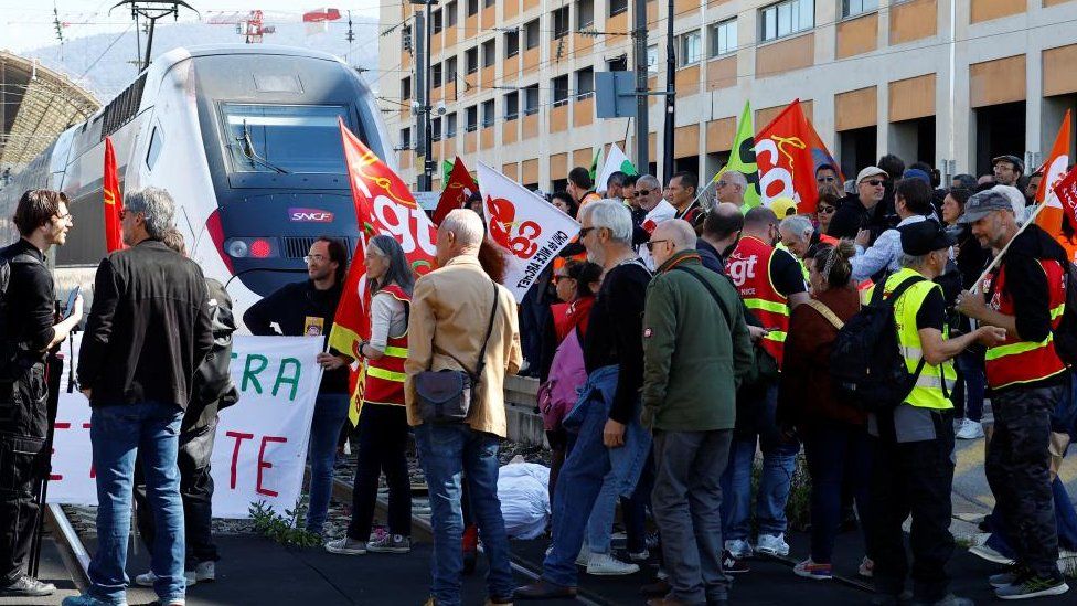 Бастующие рабочие держат профсоюзные флаги CGT, идя по железной дороге пути для блокировки скоростного поезда TGV во время демонстрации на вокзале накануне девятого дня национальной забастовки и протестов