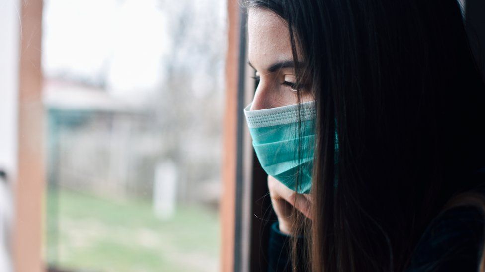 Woman with surgical mask looks out of a window