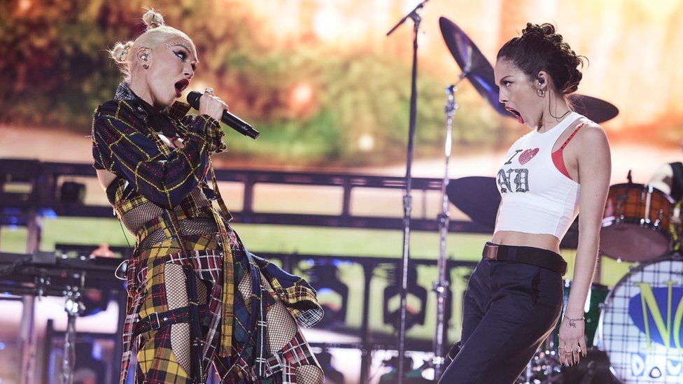Gwen Stefani and Olivia Rodrgio performing at Coachella - the pair are singing at each other. Gwen is wearing a tartan outfit, while Olivia is wearing an 'I heart ND' t-shirt