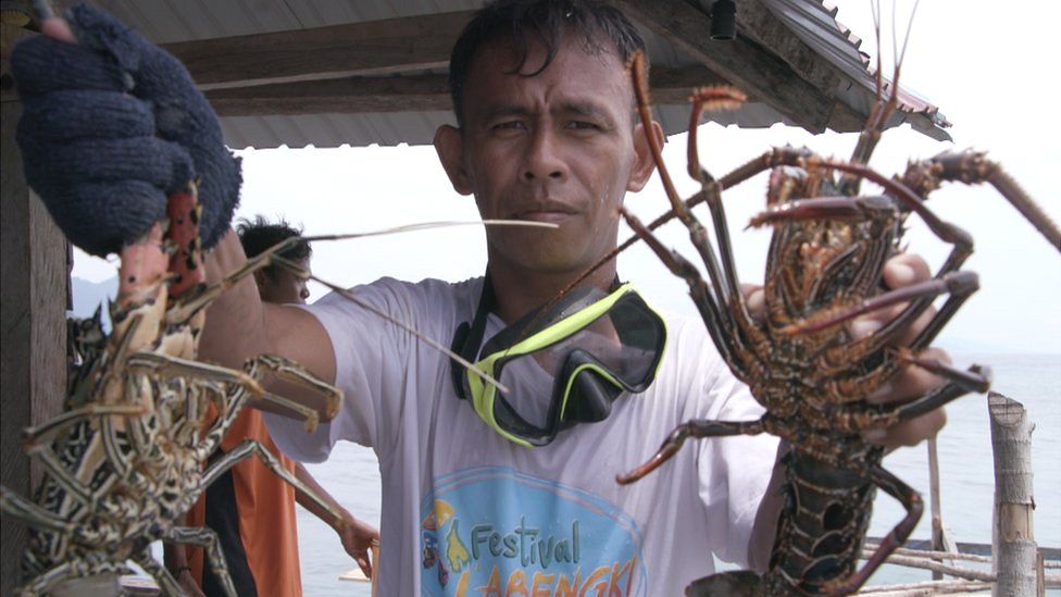 Tawing holding a lobster in each hand