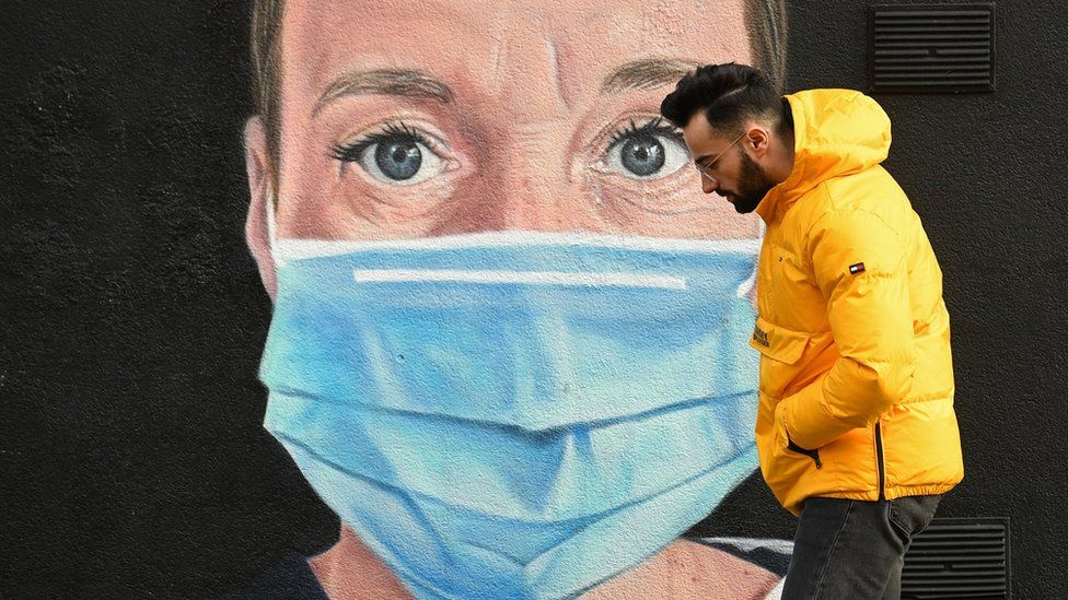 A man wearing walks past street art of an NHS worker in Manchester on 5 January 2021