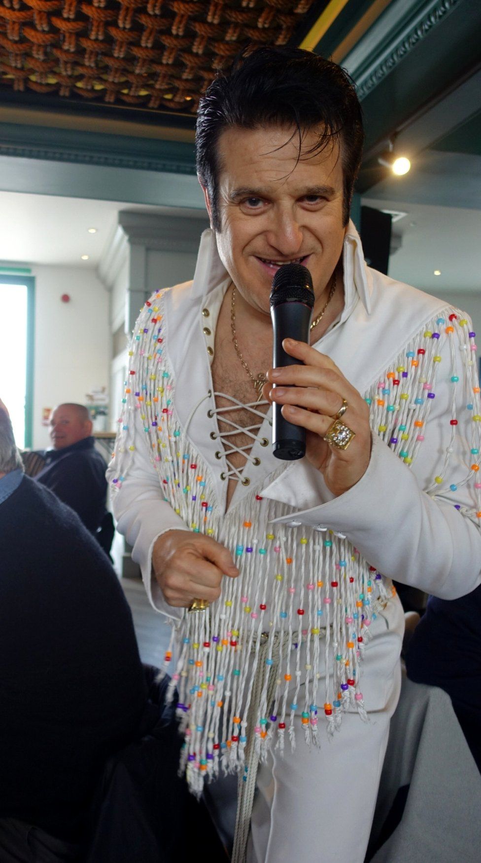 An Elvis impersonator dressed in frills holding a microphone to his lips