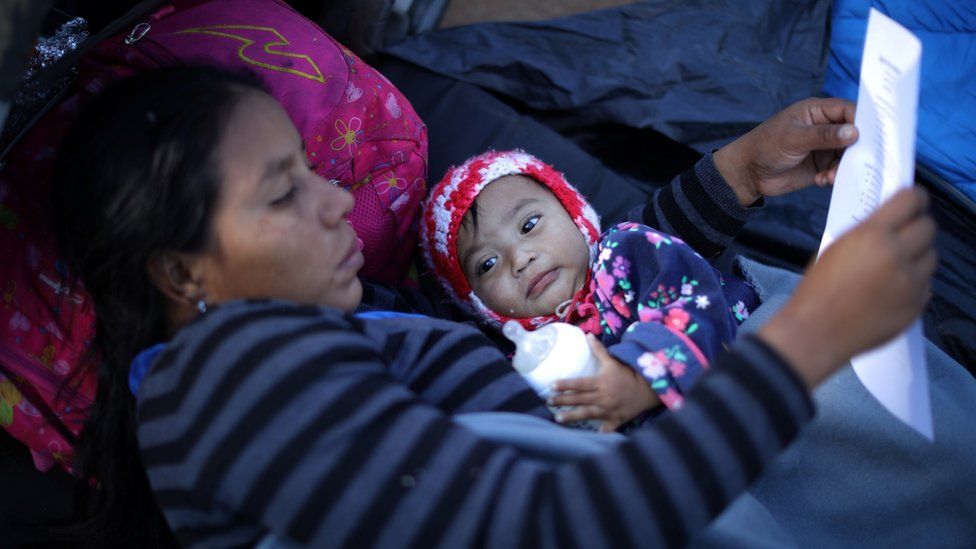 Lila lies with her 10-month-old daughter Sofia from Honduras and reads information about claiming asylum in the US as she rests in a temporary shelter in Tijuana, Mexico, 23 November