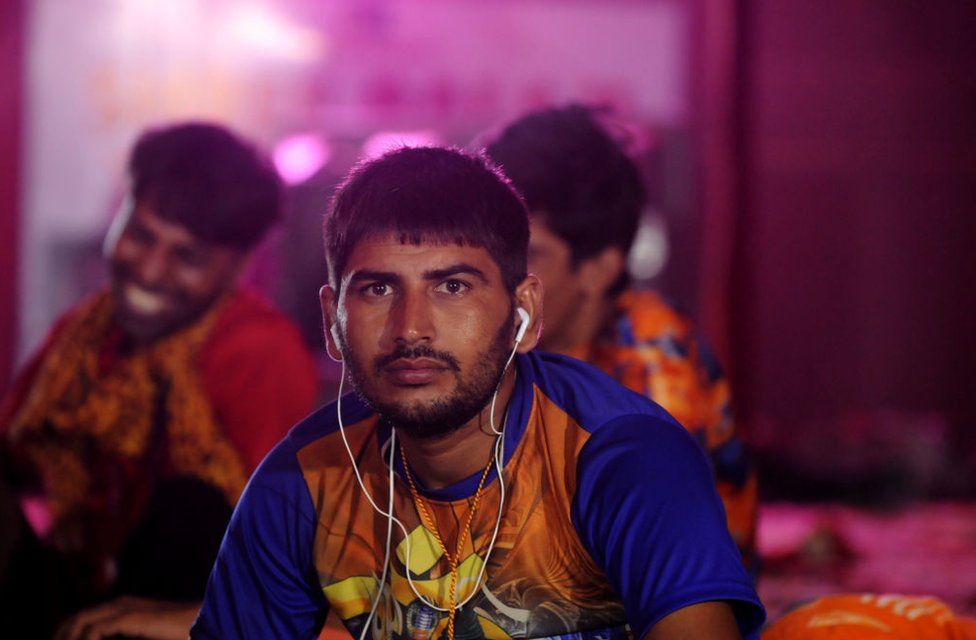 A Kanwariya rests while listening to music on his phone as others dance to religious songs at a camp in Delhi on 7 August 2018.