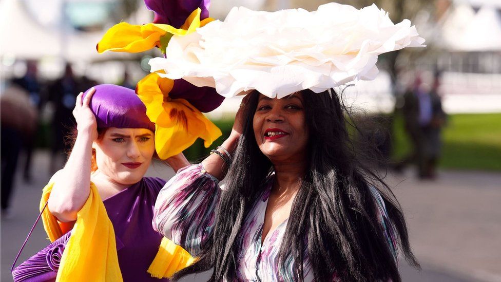 Two women holding onto their headwear at Aintree Ladies Day 2024