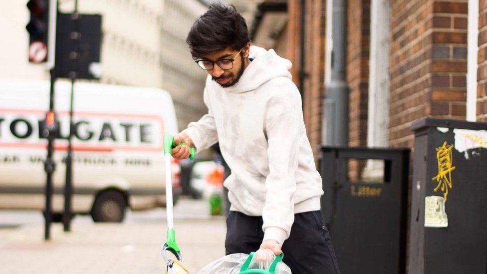 Young man in a white hoodie picking up litter with a grabbing device