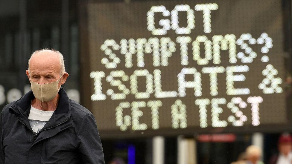 man in facemask in front of sign reading: got symptoms? isolate and get a test