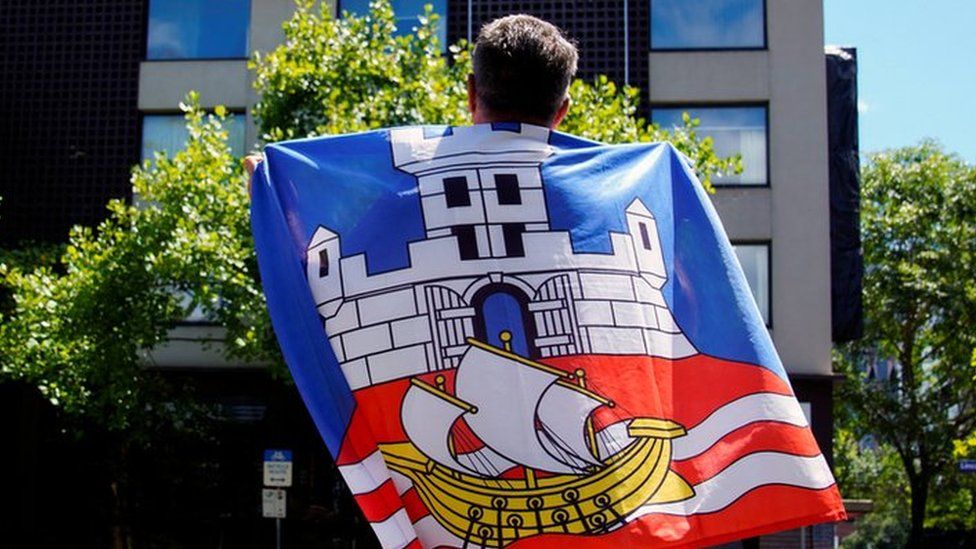 A fan draped in the Serbian flag looks up at the Park Hotel in Melbourne where Novak Djokovic has reportedly been detained