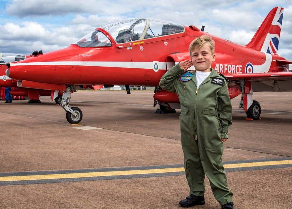 Boy saluting in front of a Red Arrow Hawk jet