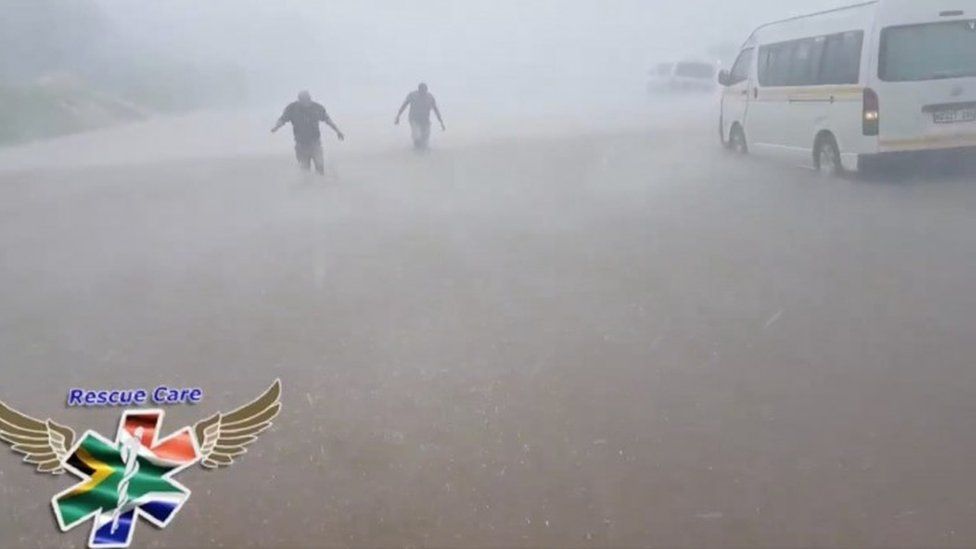 People wade through flood water in strong winds and rain next to submerged vehicles on a road during stormy weather in Durban, South Africa , 10 October 2017