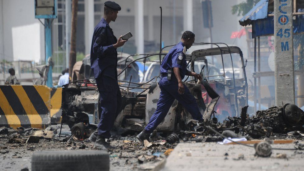 Somali security force personnel walk near the wreckage of a burnt-out vehicles at the site of a car bomb explosion near the building of the Interior Ministry in Mogadishu on July 7, 2018
